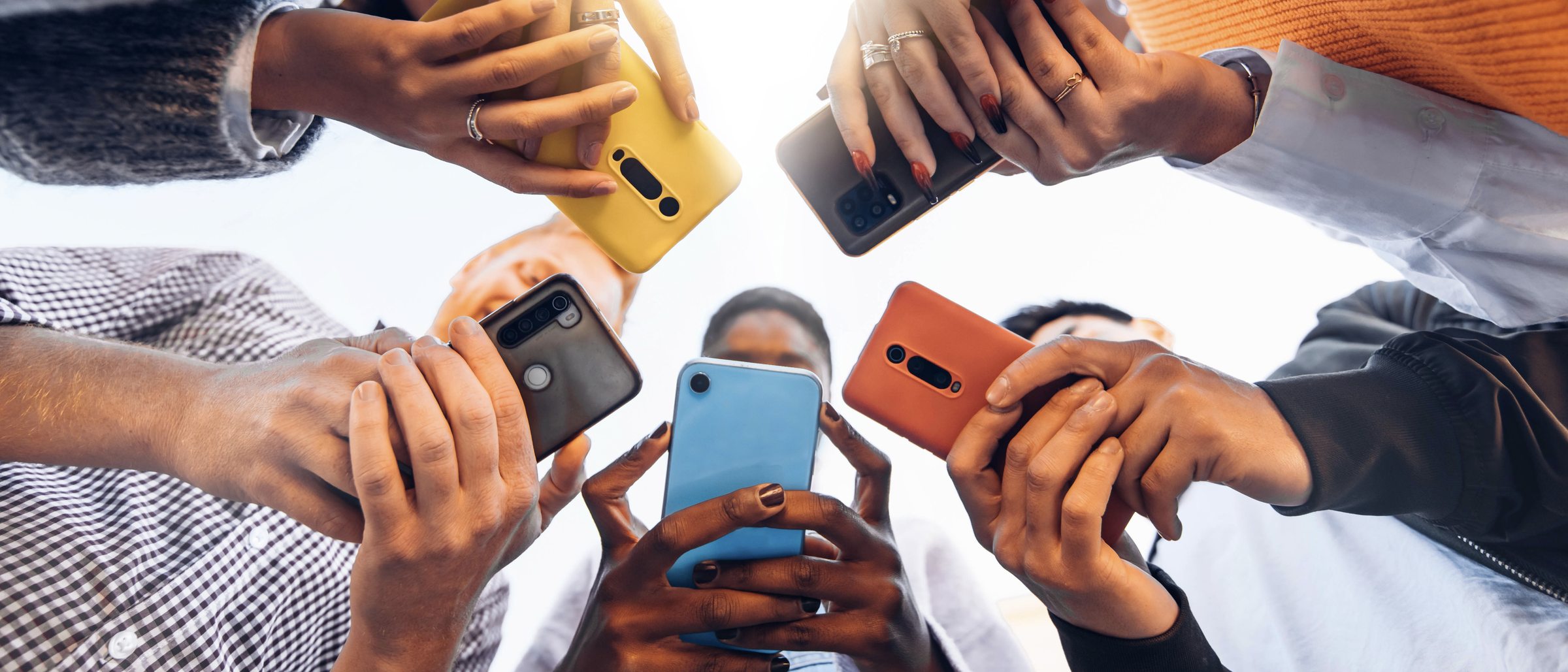 Mehrere Menschen im Kreis, jede mit Smartphone in der Hand, von unten fotografiert